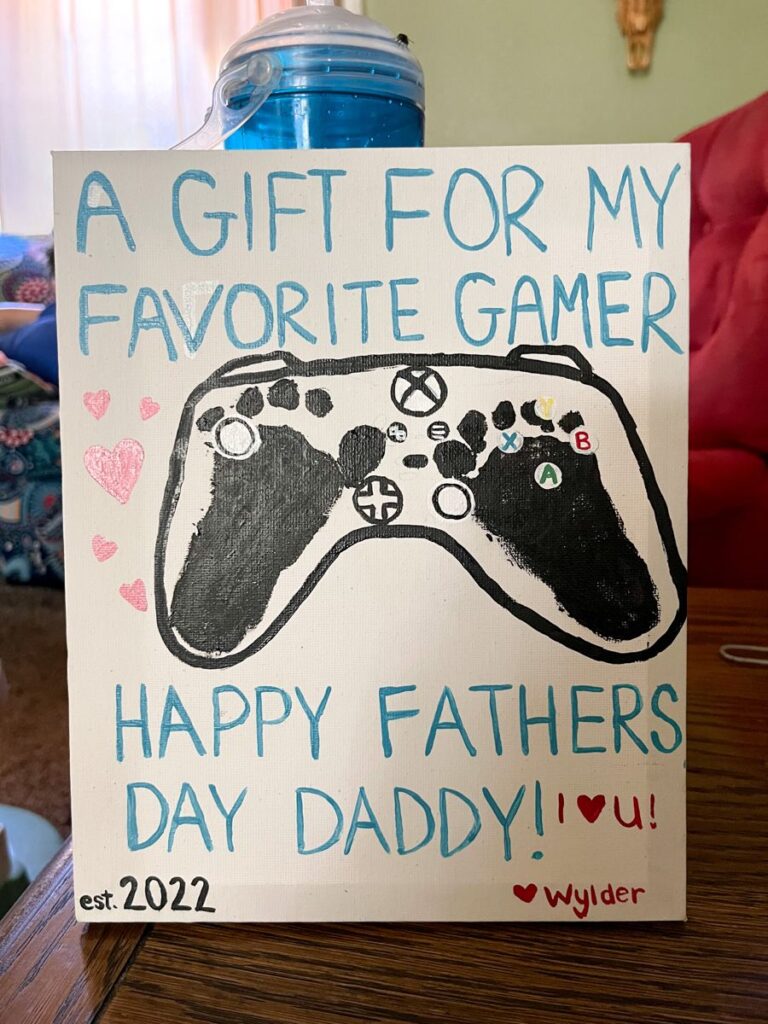 Gamer-Gift A sign has two black footprints turned into a game controller. Text reads A gift for my favorite gamer.