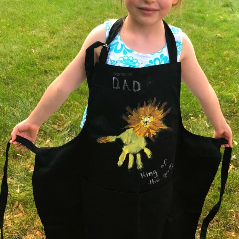 Dad-Apron A child is seen wearing a black apron with a handprint design on it
