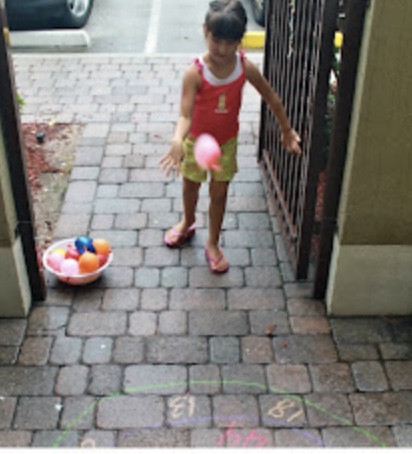 Water Balloon Activity girl throwing water balloons at numbers written in chalk on the pavement for a water activity