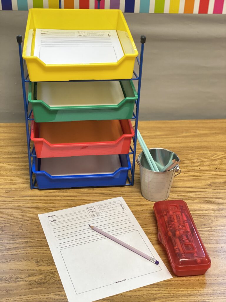 Writing area with colored bins in a kindergarten classroom.