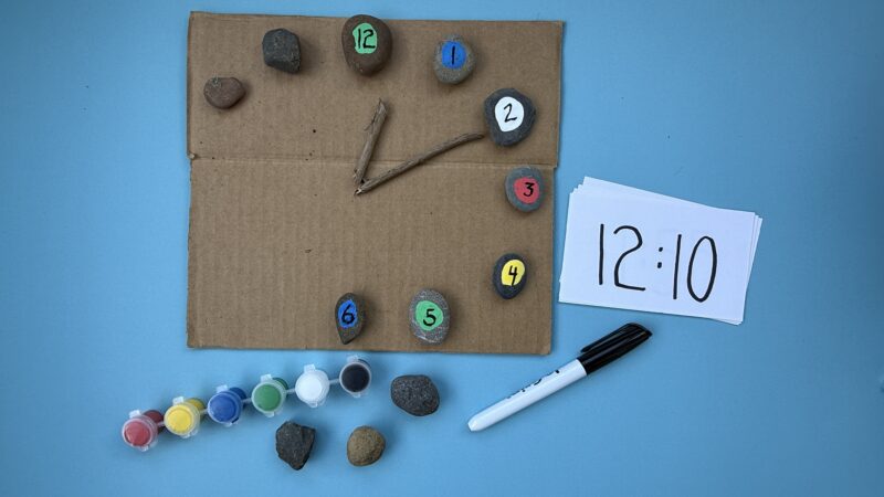 piece of cardboard with rocks and clock hands telling time
