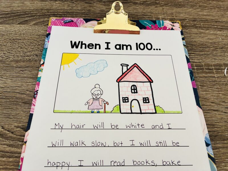 a floral clipboard holding a paper with the writing prompt: When I am 100... and a student response and drawing of themselves at 100