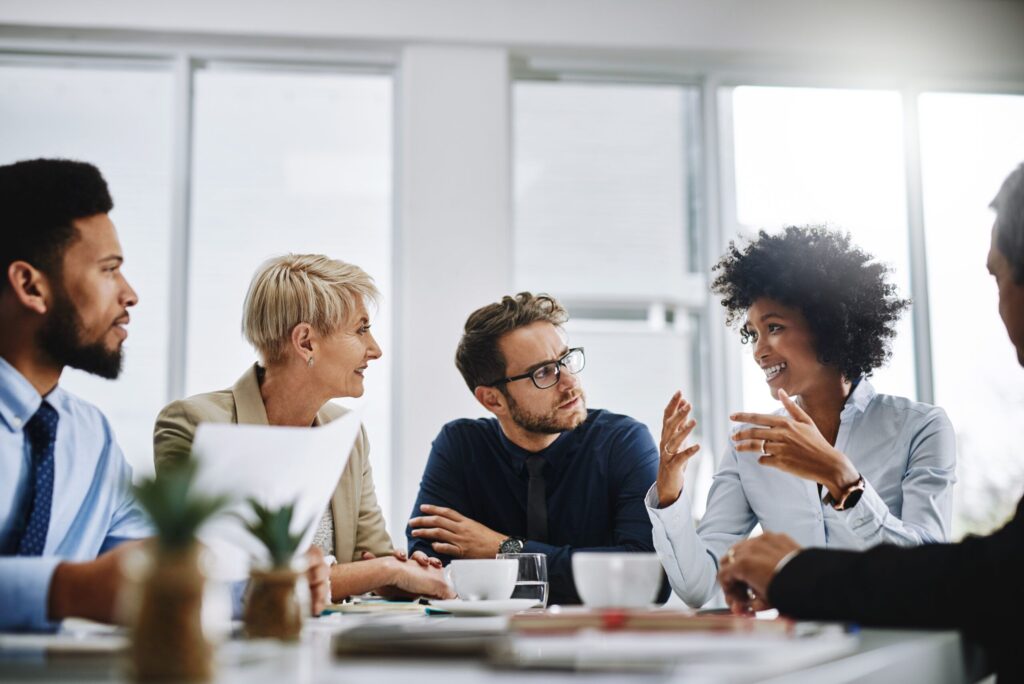 A group of professionals seated a table in an office looking at a colleague who is speaking.
