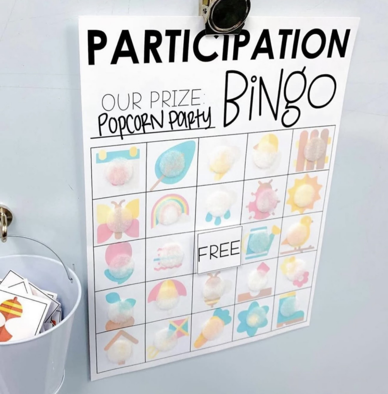 Participation Bingo page hanging on a wall next to a bucket of bingo cards
