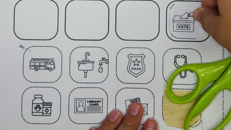 Close up of student hands doing a community helper cut and paste worksheet.